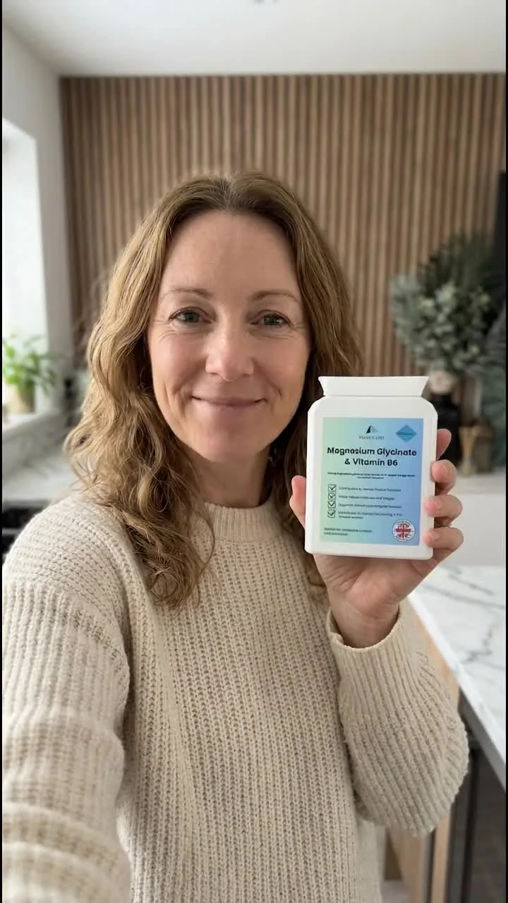 A woman in a cream jumper holding a Pulse & Pine Magnesium Glycinate & Vitamin B6 tub in a bright kitchen
